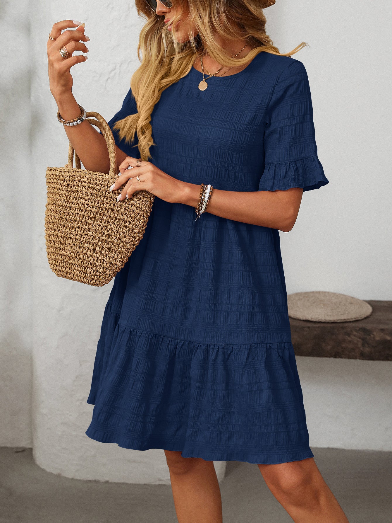 Melba Lane – Studland navy blue textured tiered short-sleeve dress, three-quarter front view with a straw tote and arm raised, AU women's sizes