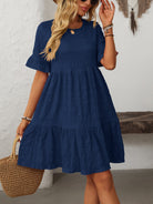 Melba Lane – Studland navy blue textured tiered short-sleeve dress, front view with a straw tote and hand raised to hair, AU women's sizes