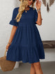 Melba Lane – Studland navy blue textured tiered short-sleeve dress, front view with a straw tote and hand raised to hair, AU women's sizes