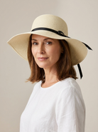 Faye Foldable Wide Brim Sun Hat in Beige worn by a confident woman in a clean studio setting.