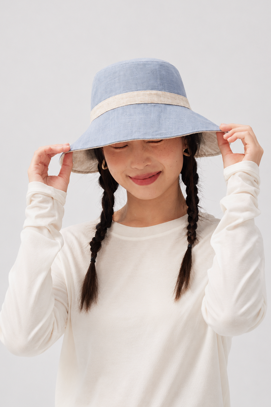 Melba Lane – Tinos light blue reversible sun hat with a natural linen band, front view with both hands on the wide brim
